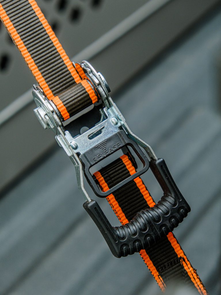 Service-2-min Durable ratchet strap with orange accents, ideal for secure cargo fastening.